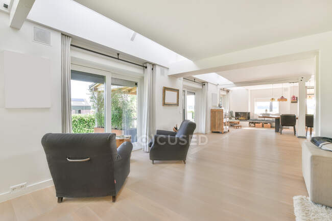 Moderno salón interior con sillones contra plantas y mesa en parquet en casa durante el día - foto de stock