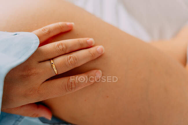 De cima da colheita fêmea irreconhecível no anel com pedra preciosa tocando a perna com pele delicada em casa — Fotografia de Stock