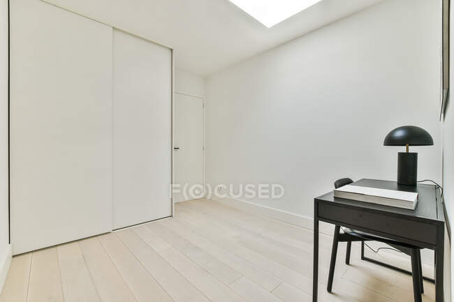Quarto contemporâneo interior com lâmpada sobre mesa preta contra porta e armário em parquet em casa de luz — Fotografia de Stock