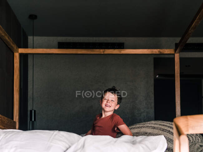 Positives kleines Kind auf hölzernem Himmelbett, während es im Schlafzimmer Spaß hat und in die Kamera schaut — Stockfoto