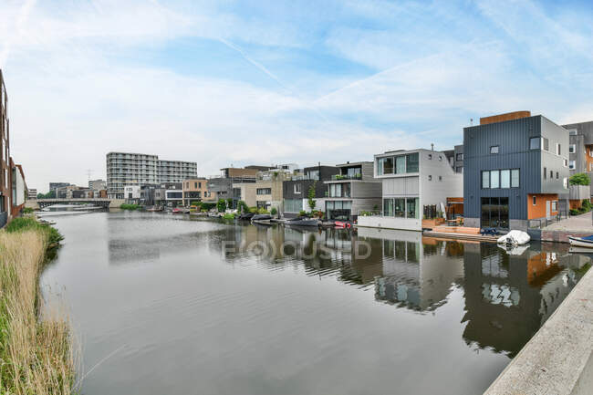 Contemporary house exteriors reflecting in rippled river under bridge and cloudy sky in Amsterdam Holland — Stock Photo