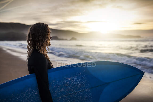 Перед тим як пірнути у море під час заходу сонця на пляжі в Астурії (Іспанія), на березі видніється нерозпізнана молода жінка. — стокове фото