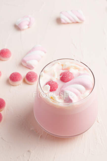 Glass of sweet hot white chocolate with pink jelly candies and marshmallow served on white table — Stock Photo