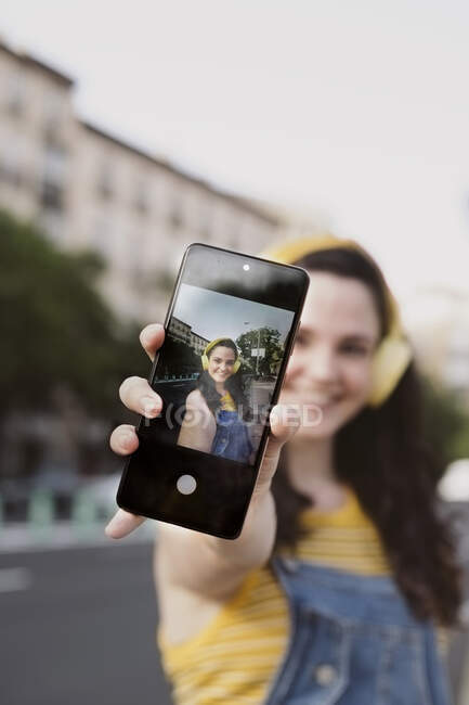 Femme insouciante dans les écouteurs sans fil prendre selfie sur téléphone portable dans la rue — Photo de stock