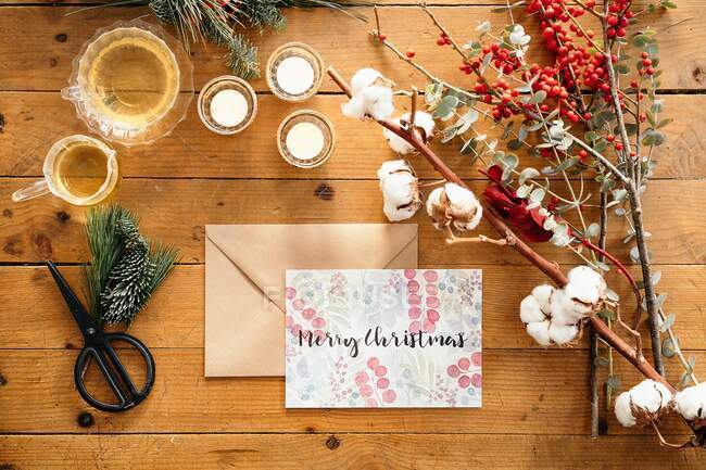 Ansicht von Weihnachten Komposition mit bunten Postkarte mit der Aufschrift Feliz Navidad in der Nähe brennenden Kerzen und Tassen Tee auf Holztisch mit bunten Zweigen von Pflanzen dekoriert platziert — Stockfoto