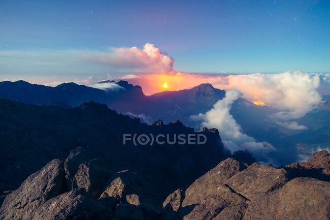 Ночной пейзаж с извергающимся вулканом на заднем плане и морем облаков, покрывающим горы с вершины скалистой горы. Извержение вулкана Кумбре-Вьеха на Канарских островах, Испания, 2021 г. — стоковое фото