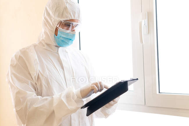 Attentive male medic in personal protective equipment touching screen on tablet during COVID 19 pandemic in clinic — Stock Photo