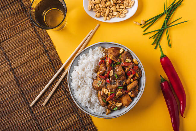 Vista superior da tigela de composição com frango kung pao com amendoim de arroz branco e pimenta vermelha quente e cebola verde e pauzinhos — Fotografia de Stock