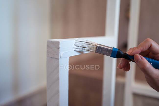 Vista lateral da fêmea irreconhecível cortada com quadro de grade de pintura de escova acima escadas em casa — Fotografia de Stock