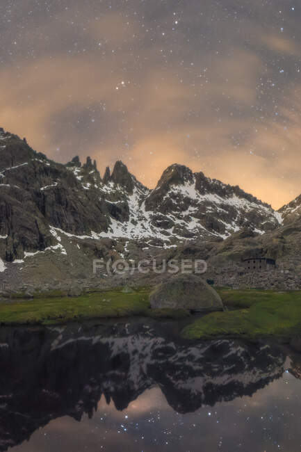 Cenário pitoresco de altas montanhas rochosas cobertas de neve refletindo na água calma do rio abaixo do céu noturno estrelado — Fotografia de Stock