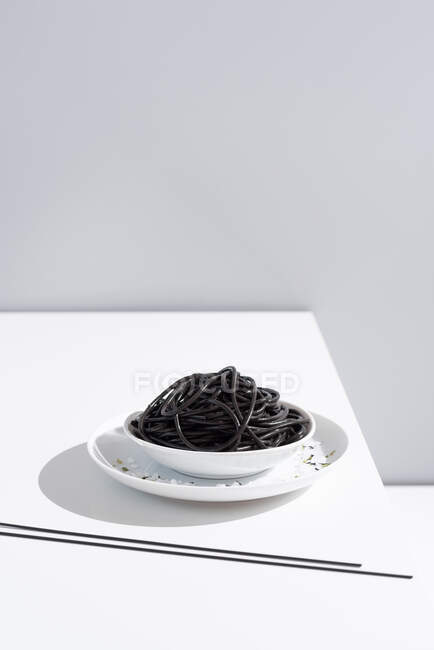 From above of ceramic bowl with delicious spaghetti with black squid ink with chopsticks on grey background — Stock Photo