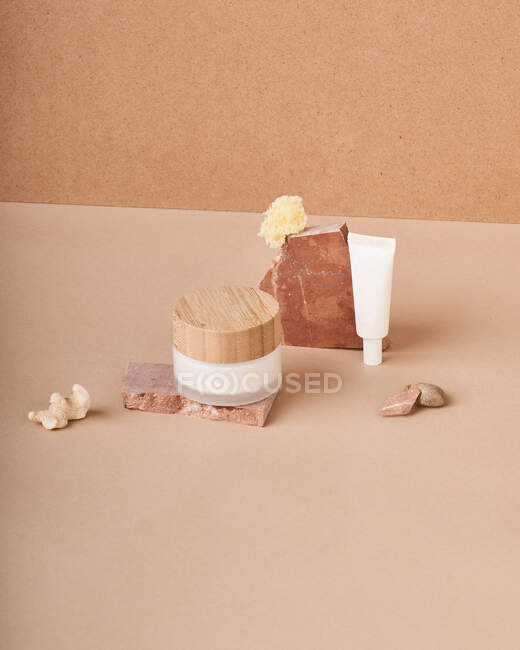 Tarro y tubo de crema con piezas de jabón orgánico hechas a mano cerca de piedra pómez sobre fondo de dos colores - foto de stock