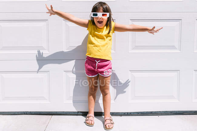 Cheerful cute girl in casual colorful clothes and three dimensional glasses standing on white wall background — Stock Photo