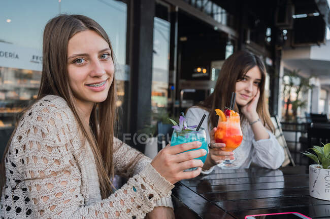 Crop content best female friends with tasty beverages looking at camera in street cafeteria — Stock Photo