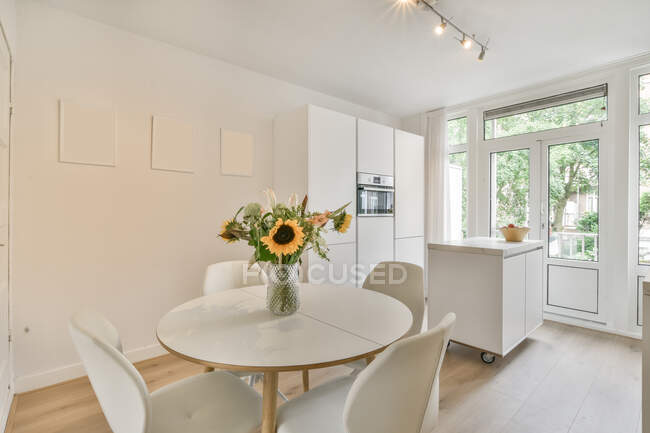 Mesa redonda com buquê de flores colocadas perto da cozinha leve no apartamento moderno durante o dia — Fotografia de Stock