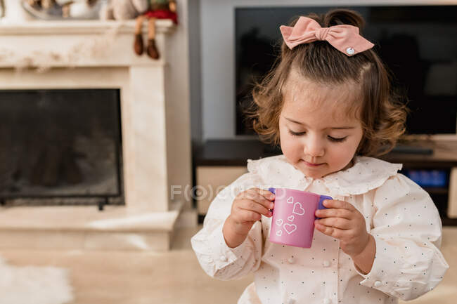 Zufriedenes Kleinkind mit Schleife am Haar spielt im Wohnzimmer mit Plastikspielzeug — Stockfoto