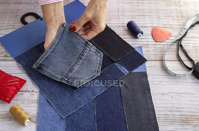 Сверху анонимный портной, надевающий джинсовый карман на кусочки ткани, пока шьет джинсы в ателье — стоковое фото