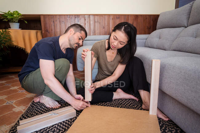Pareja multirracial montando mesa sobre alfombra en casa - foto de stock