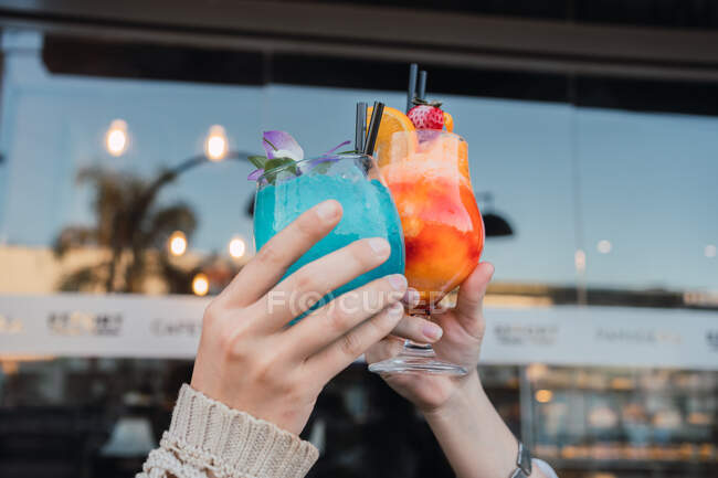 Anónimo alegre hembra adolescentes interactuando mientras tintineo vasos de deliciosas bebidas refrescantes en la mesa en la cafetería urbana - foto de stock