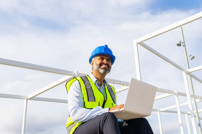 From below delighted male supervisor in uniform working on netbook while sitting near solar power station — Stock Photo