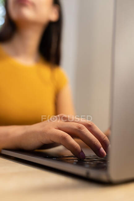 Cropped unrecognizable young female entrepreneur sitting at table and browsing netbook while working on modern workplace — Stock Photo