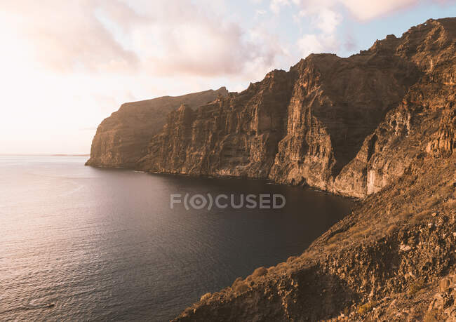 Scenery view of high dry mountain against endless ocean under cloudy sky at sunset in Tenerife Spain — Stock Photo