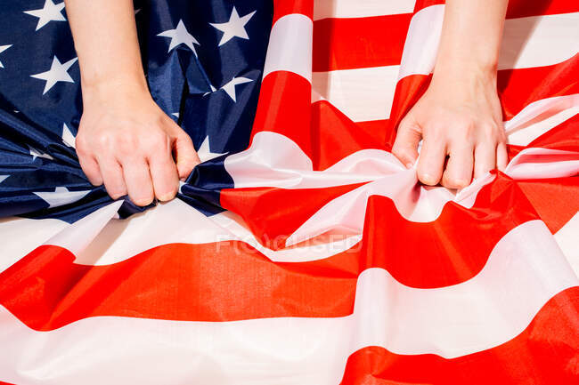 Ângulo elevado da colheita pessoa irreconhecível que toca a bandeira vincada de América com o ornamento da estrela e da faixa — Fotografia de Stock