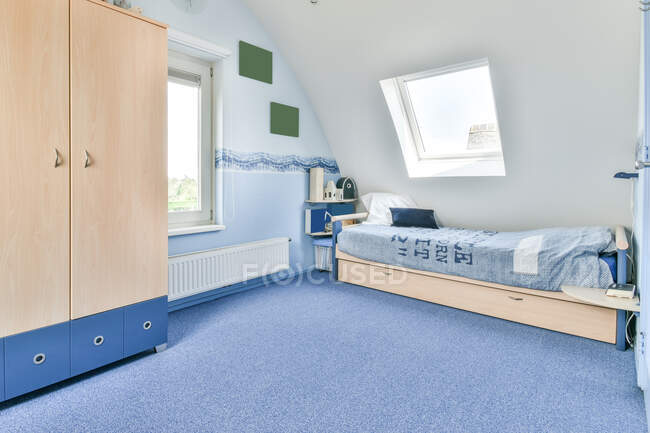Diseño creativo de dormitorio con armario contra cama y radiador bajo ventana en casa a la luz del día - foto de stock