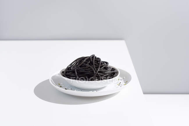 Estúdio minimalista com espaguete de tinta de lula preta em tigela de cerâmica completa na mesa branca — Fotografia de Stock