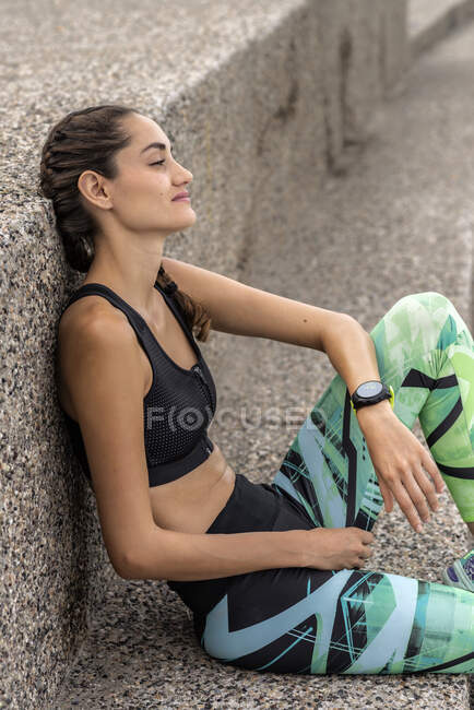Atlético feminino corredor no sportswear inclinado no parede enquanto tomando pausa durante o treino no cidade — Fotografia de Stock