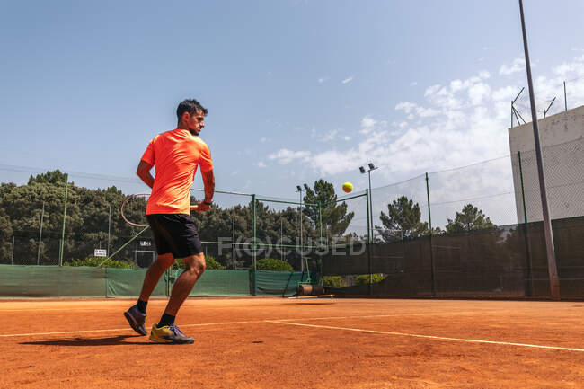 Hombre adulto en ropa deportiva jugando al tenis en un día soleado en la cancha - foto de stock
