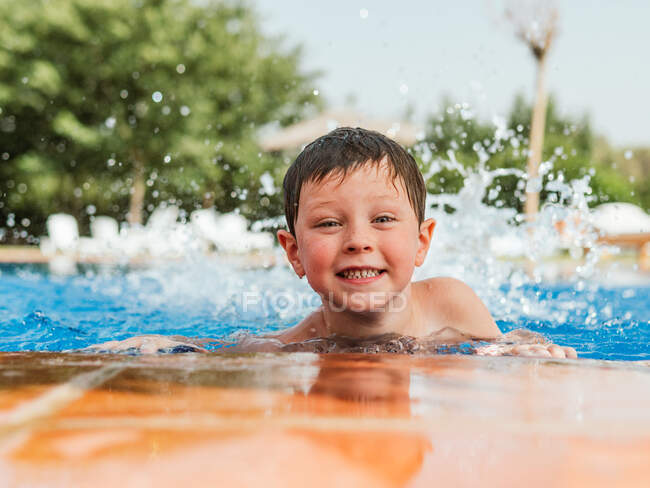 Entzücktes süßes Kind mit nassen Haaren, das am Pool lehnt und in die Kamera schaut, während es am Sommerwochenende Spaß hat — Stockfoto