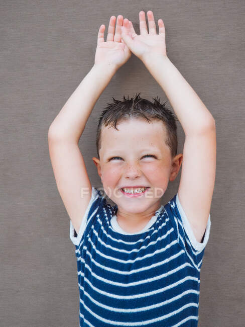 Sonriente chico con el pelo mojado usando camiseta rayada mirando a la cámara contra la pared de madera - foto de stock