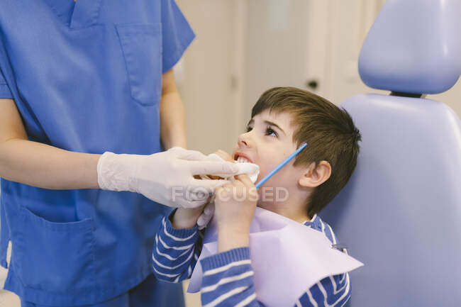Ortodontista delle colture in uniforme e guanti mettendo strumento dentale nella cavità orale del ragazzo durante l'appuntamento in clinica — Foto stock