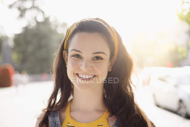 Jovem fêmea feliz com cabelos castanhos compridos vestindo ganga em geral de pé olhando para a câmera com sorriso — Fotografia de Stock