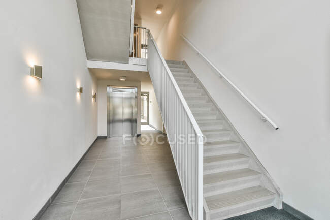 Moderno interior de amplio pasillo con escalera y ascensor con puertas metálicas en edificio residencial moderno - foto de stock