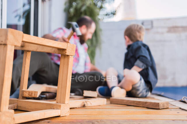Anonymous father with boy working with wooden pieces while sitting on boardwalk and interacting in daytime — Stock Photo