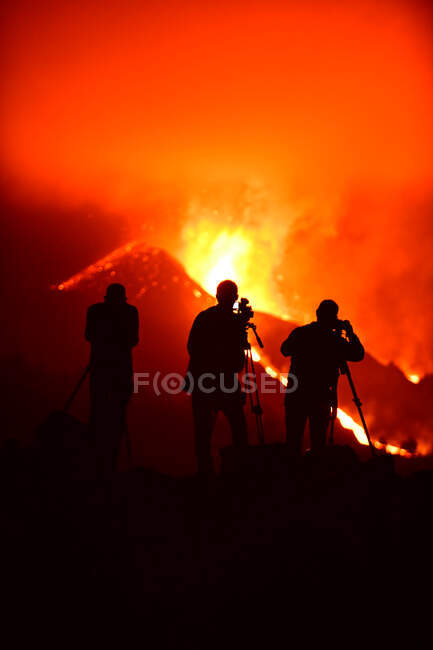 Siluetas humanas de los medios grabando y fotografiando con trípodes la explosión de lava en La Palma Islas Canarias 2021 - foto de stock