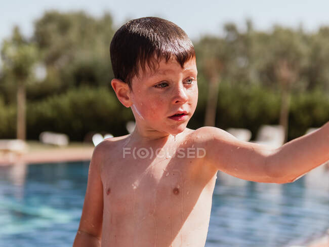 Liebenswertes kleines Kind mit nassen Haaren genießt das Wochenende am Pool an einem sonnigen Tag im Sommer und schaut weg — Stockfoto