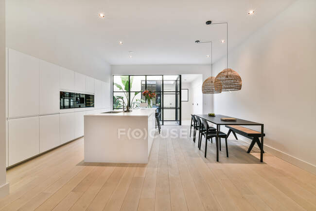 Table under lamps against built in electric appliances in contemporary kitchen in house with parquet — Stock Photo