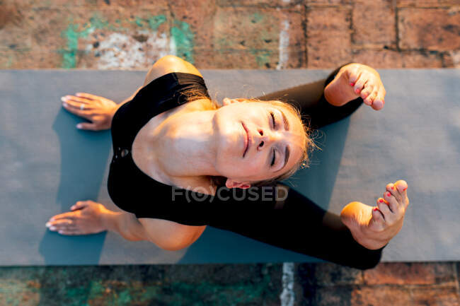 Young slender female in sports clothes doing Raja Bhujangasana while practicing yoga in city on sunny day — Stock Photo