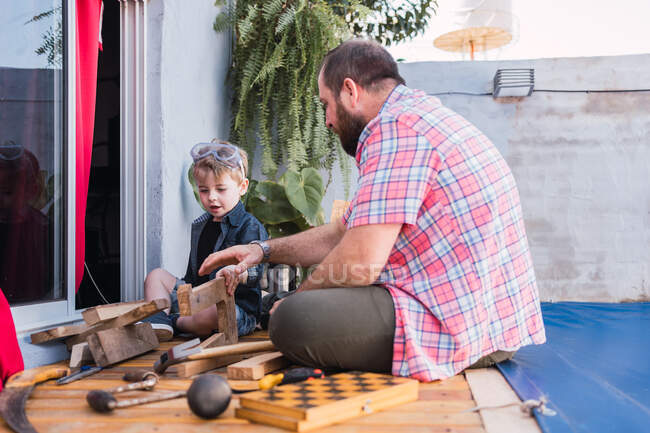 Nível do solo de pai barbudo alegre em camisa quadriculada com menino trabalhando com blocos de madeira — Fotografia de Stock