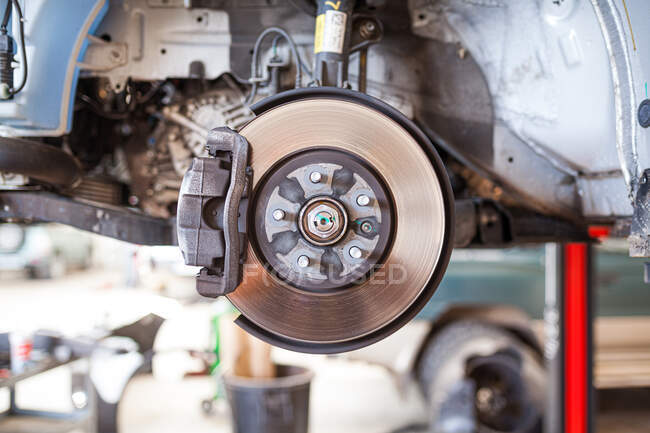 Крупный план металлического дискового тормоза автомобиля, установленного на лифте в ремонтной службе — стоковое фото