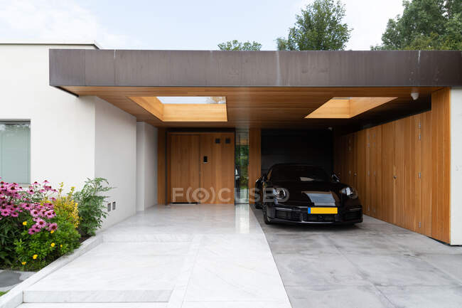 Modern sport car parked in backyard of stylish minimalist villa decorated with blooming plants on sunny day — Stock Photo