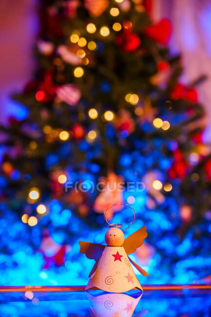 Giocattolo a forma di angelo fatto a mano posto sul tavolo riflettente contro l'albero di Natale festivo con ghirlande incandescenti — Foto stock