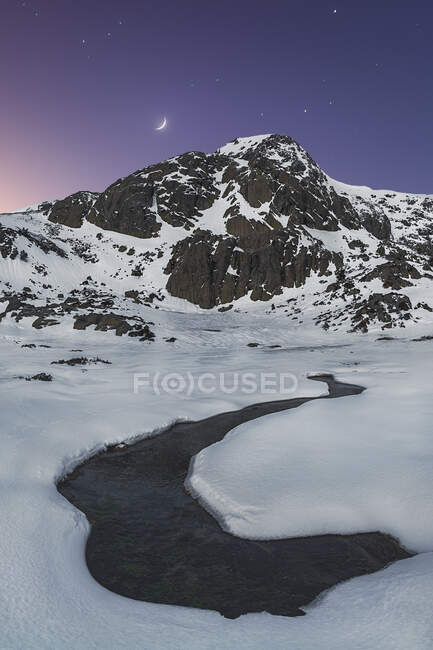 Cenário pitoresco de rio frio fluindo entre vale nevado levando a alta montanha rochosa sob céu estrelado ao entardecer — Fotografia de Stock