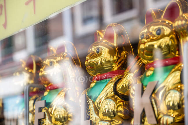 A través de la vista de la pared de cristal de las figurillas tradicionales japonesas de los gatos de señas de cerámica dorada en la ciudad - foto de stock