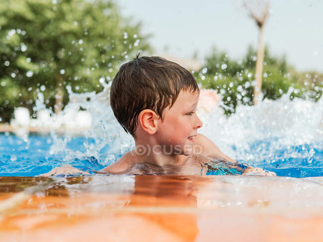 Entzücktes süßes Kind mit nassen Haaren, das am Pool lehnt und Spaß am Sommerwochenende hat — Stockfoto