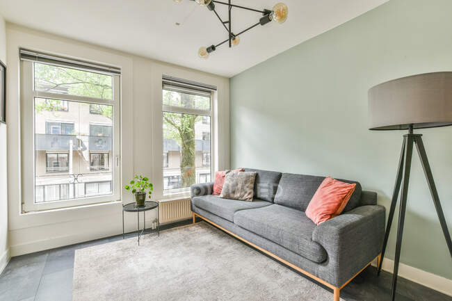 Couch mit Kissen zwischen Tisch mit Topfpflanze und Lampe auf dem Boden in zeitgenössischem Raum tagsüber zu Hause — Stockfoto