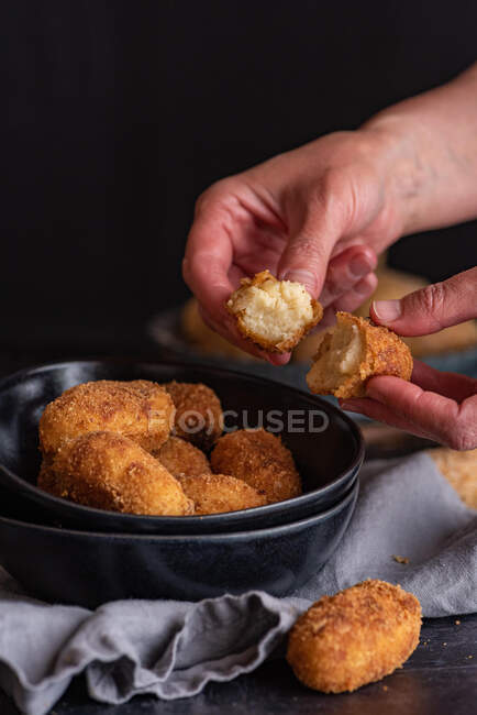 Crop unrecognizable person demonstrating half of yummy deep fried croquette with cheese filling on black background — Stock Photo
